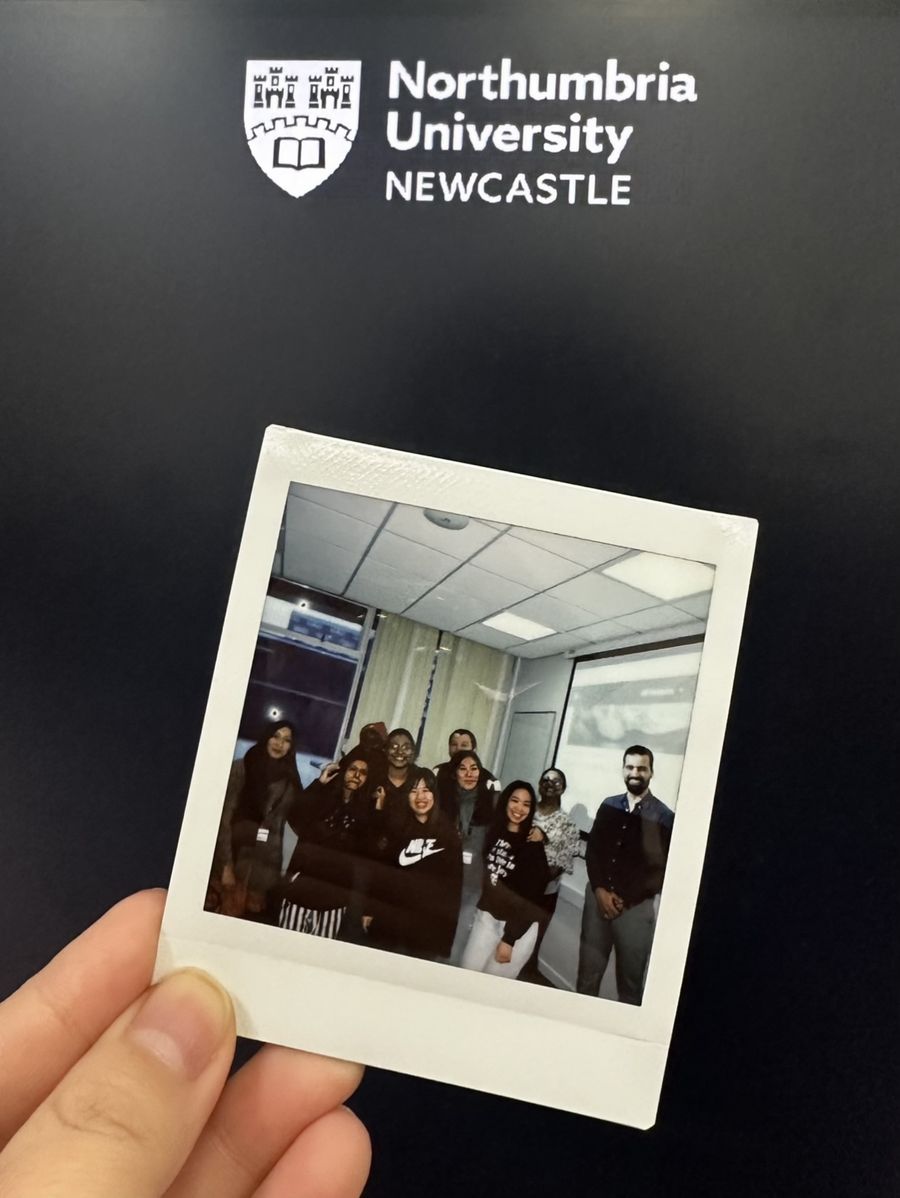 Instant photo of Rachid with his EL7038 students, held up in front of a Northumbria University sign
